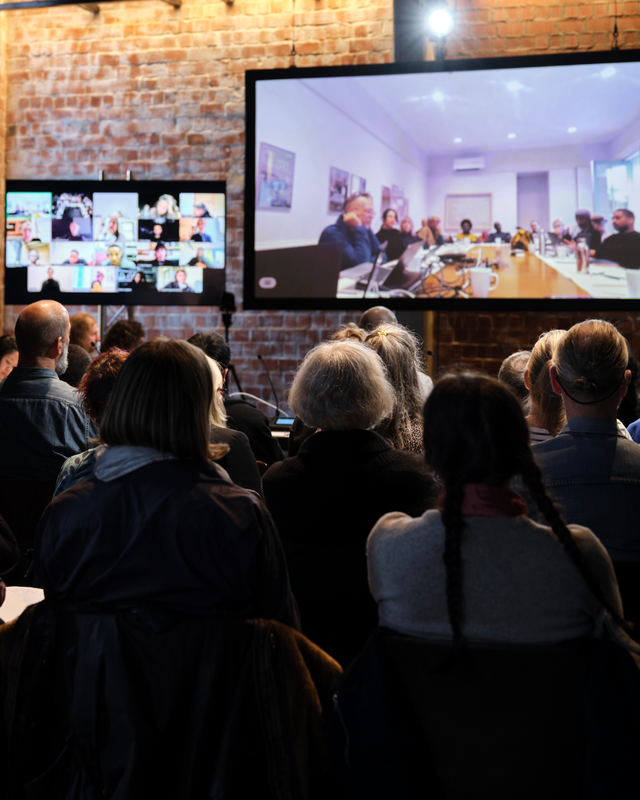 people are sat watching a conference on a screen